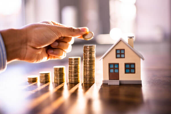 Hand stacking coins next to a small house model